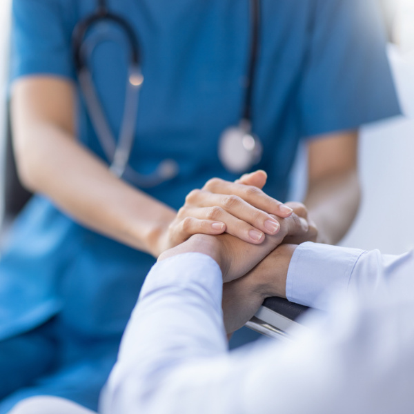 Nahaufnahme einer Ärztin in blauer Uniform mit Stethoskop, die die Hand eines Patienten hält. Nahaufnahme einer Ärztin in blauer Uniform mit Stethoskop, die die Hand eines Patienten hält.