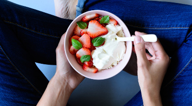 Eine Schale mit Erdbeeren und Joghurt in den Händen einer Person, die im Schneidersitz sitzt. Eine Schale mit Erdbeeren und Joghurt in den Händen einer Person, die im Schneidersitz sitzt.