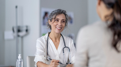 Ärztin mit Stethoskop lächelt und führt ein medizinisches Beratungsgespräch mit einer Patientin, die im Vordergrund sitzt. Ärztin mit Stethoskop lächelt und führt ein medizinisches Beratungsgespräch mit einer Patientin, die im Vordergrund sitzt.