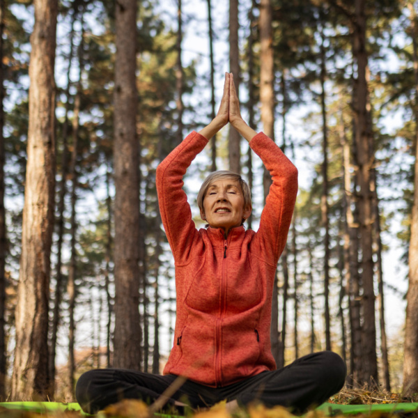Ältere Frau mit roter Jacke sitzt im Schneidersitz im Wald und macht Yoga. Ältere Frau mit roter Jacke sitzt im Schneidersitz im Wald und macht Yoga.