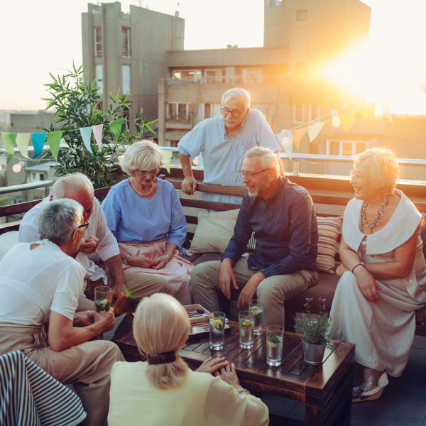 Eine Gruppe von Senioren, die auf einer Terrasse bei Sonnenuntergang zusammensitzen und sich am Tisch unterhalten. Eine Gruppe von Senioren, die auf einer Terrasse bei Sonnenuntergang zusammensitzen und sich am Tisch unterhalten.