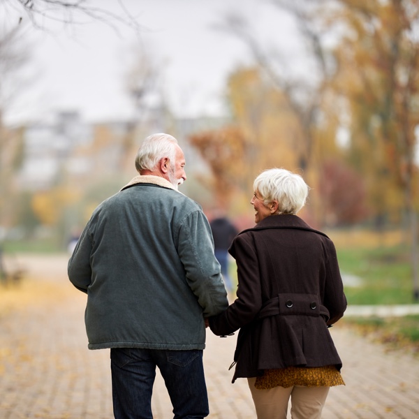 Ansicht eines älteren Paars von hinten. Sie spazieren im Herbst Hand in Hand durch einen Park und schauen sich lächelnd an. Ansicht eines älteren Paars von hinten. Sie spazieren im Herbst Hand in Hand durch einen Park und schauen sich lächelnd an.