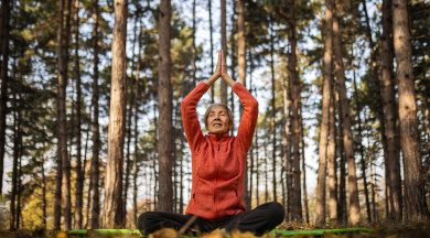 Ältere Frau mit roter Jacke sitzt im Schneidersitz im Wald und macht Yoga. Ältere Frau mit roter Jacke sitzt im Schneidersitz im Wald und macht Yoga.