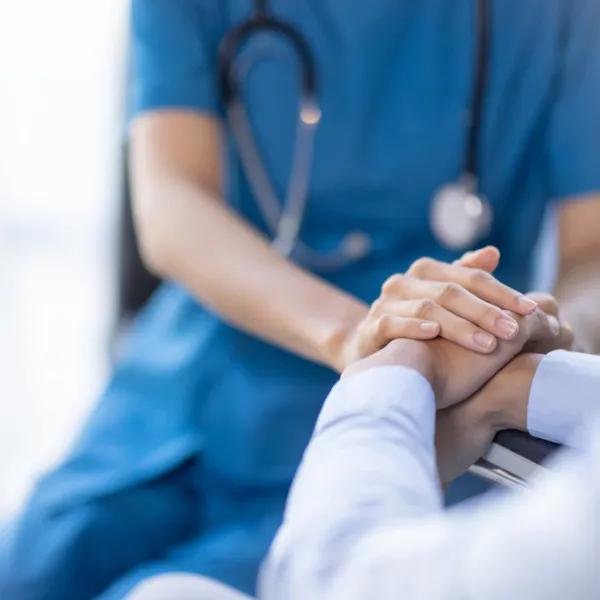 Nahaufnahme einer Ärztin in blauer Uniform mit Stethoskop, die die Hand eines Patienten hält.